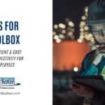 A blog post graphic titled "TABLETS FOR THE TOOLBOX" in large blue text. Below, smaller grey text reads "RELIABLE, EFFICIENT & COST-EFFECTIVE CONNECTIVITY FOR WORKPLACE EMPLOYEES". To the right, a slightly blurred image shows a worker wearing a hard hat and safety vest, looking down at a tablet they are holding and making notes with a pen. The background is dark with blurred industrial lights. The "AGDisplays" logo and website address are in the bottom left corner.
