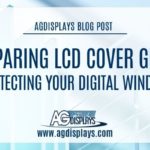 A softly focused image of stacked clear glass panels, likely LCD cover glass, with a white overlay and the text "AGDISPLAYS BLOG POST" at the top, followed by "COMPARING LCD COVER GLASS PROTECTING YOUR DIGITAL WINDOW," and the AGDisplays logo with "www.agdisplays.com" at the bottom. The overall tone is light and clean.