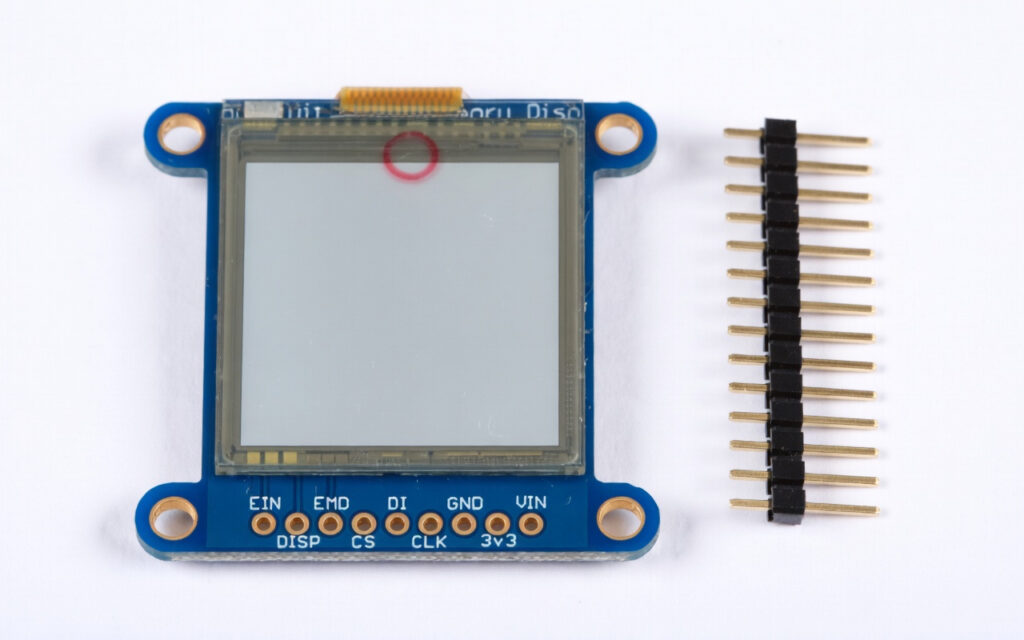 Memory-in-Pixel (MIP) LCD module on blue Arduino-compatible board with header pins, demonstrating ultra-low-power display technology for battery-powered rugged devices. Red circle highlights the reflective screen area.