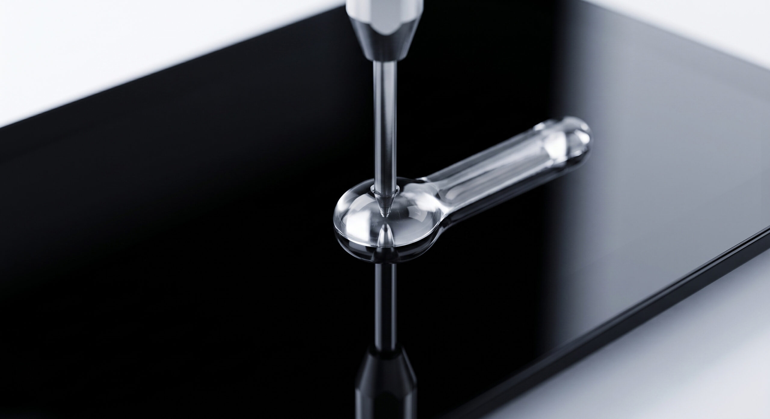 A metal dispenser tip applying a viscous, clear liquid adhesive in a distinctive pattern resembling a bone onto a glossy, reflective black glass surface against a white background. Reflections of the tool and liquid are visible in the glossy surface.